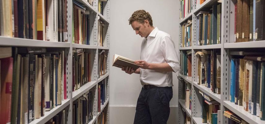 A man reading a book between two bookshelves